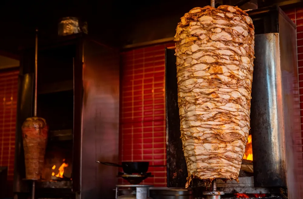 Broche de kebab tournante dorée devant les flammes, viande généreuse