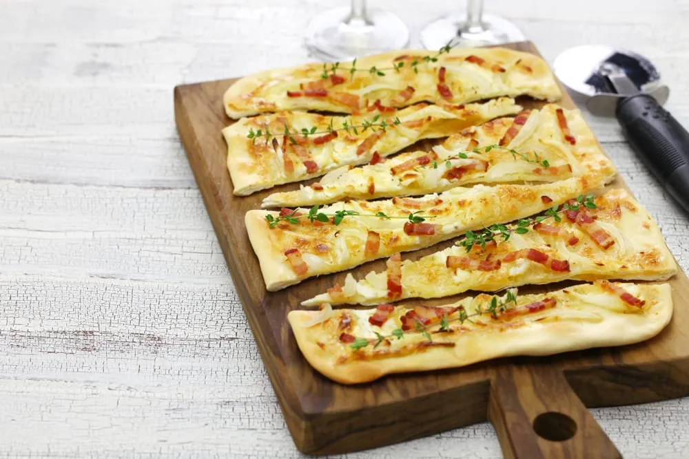 Flammekueche tradition lardons et crème fraîche découpée sur planche bois