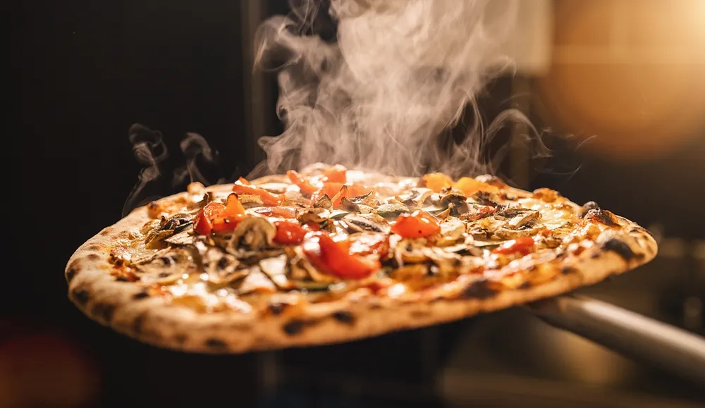 Pizza napolitaine fumante sortie du four à bois avec tomates cerises et légumes grillés