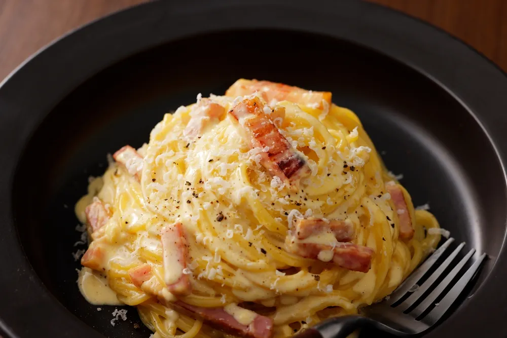Spaghetti carbonara crémeux avec lardons et parmesan râpé dans un bol noir